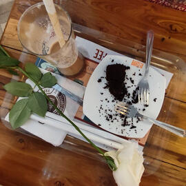remnants of a coffee and a crumbly cake with a white rose on the side